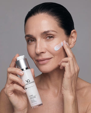 Woman applying skincare product to her face while holding a bottle of Young Goose C.A.R.E. (CARE) Anti-Aging Moisturizer in hand